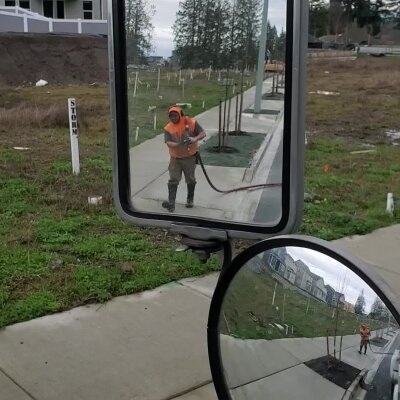 Worker reflected in vehicle side mirror on construction site.