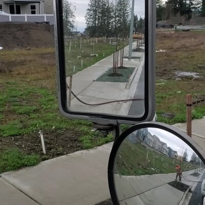 Rearview mirror reflecting person walking on suburban sidewalk.