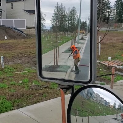 Construction worker leveling concrete viewed through vehicle side mirror.