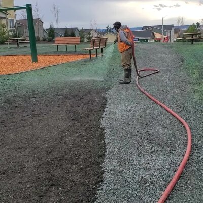 Worker spraying grass seed in playground with hose and hydroseeding equipment.
