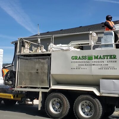Worker standing on hydroseeding truck on a sunny day.