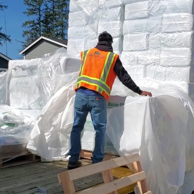 Construction worker handling plastic-wrapped materials on wooden pallets outdoors.