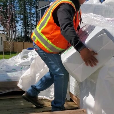 Worker in high-visibility vest carrying insulation material outdoors.