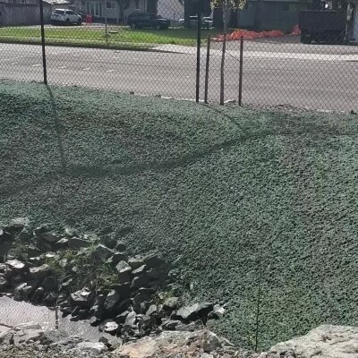 Erosion control netting on sloped ground with rocks and chain-link fence.