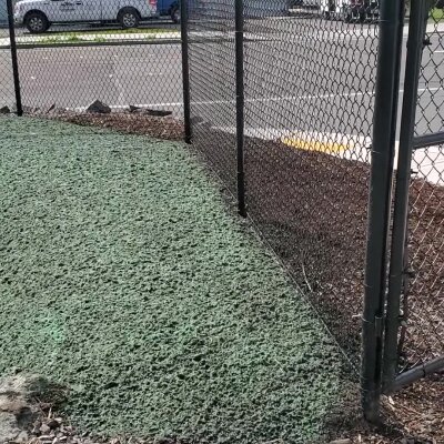 Chain-link fence corner on concrete with road and car in background.