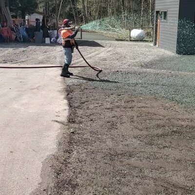 Person using a leaf blower on a gravel driveway near a building.