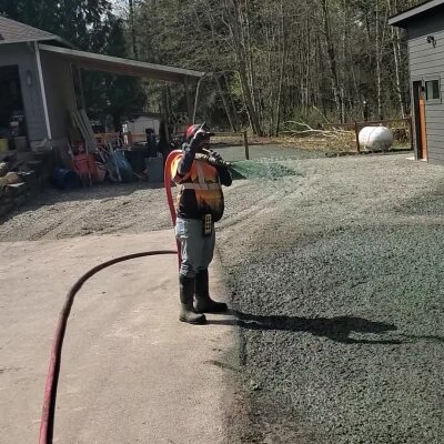 Person spraying water on a gravel driveway near a house.