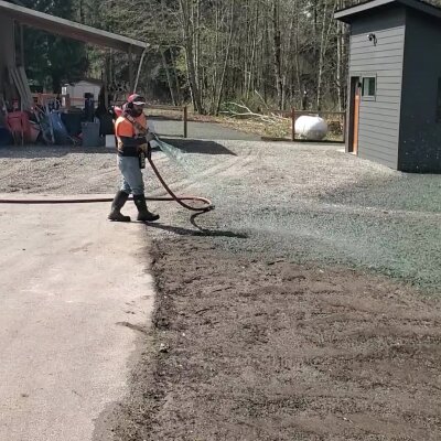 Person wearing safety gear using a hose on a gravel driveway.