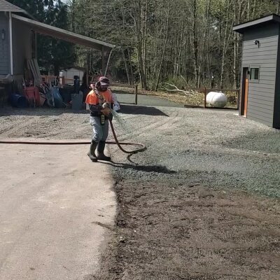 Person using leaf blower on driveway near residential buildings.