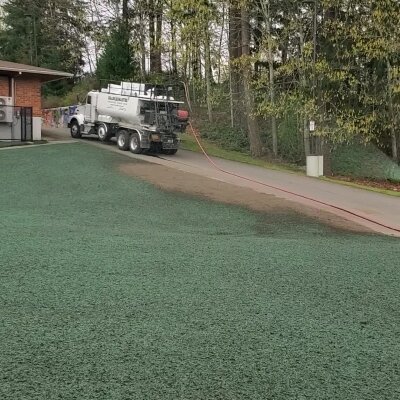 Truck spraying green hydroseed mixture on ground for landscaping.