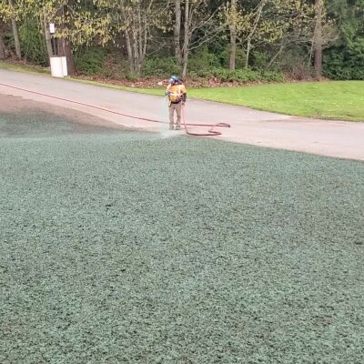 Worker spraying water on artificial grass in a park.