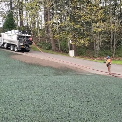 Worker spraying grass seed from truck on soil with hose.