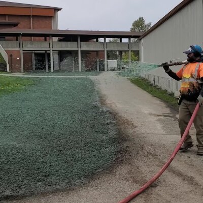 Worker spraying green hydroseed mixture for new lawn establishment.
