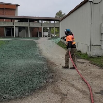 Worker spraying green hydroseed mixture on soil outdoors.