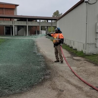 Worker spraying liquid on grass beside a building.