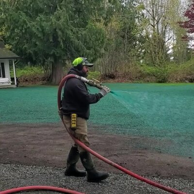 Man spraying green hydroseed mixture on soil for grass growth.