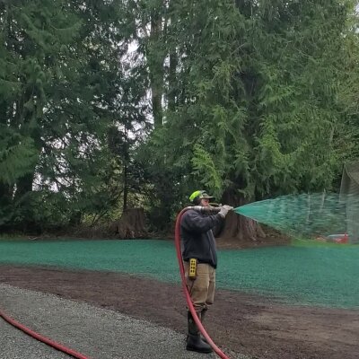 Worker watering green space with hose near trees.