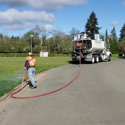 Worker using hose near industrial truck on sunny day.