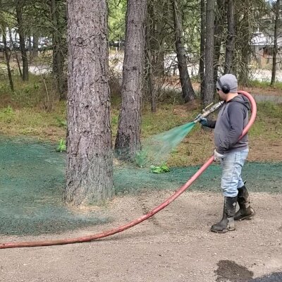 Man spraying green hydroseed mixture in forested area.