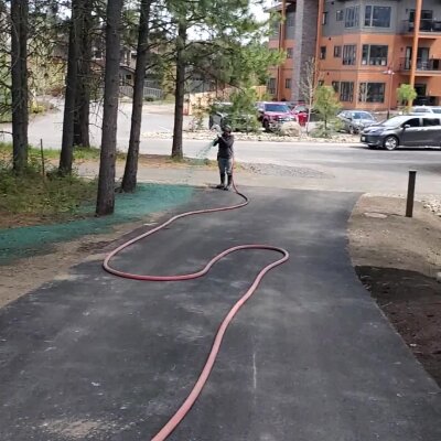 Person with hose on pathway near trees and building.