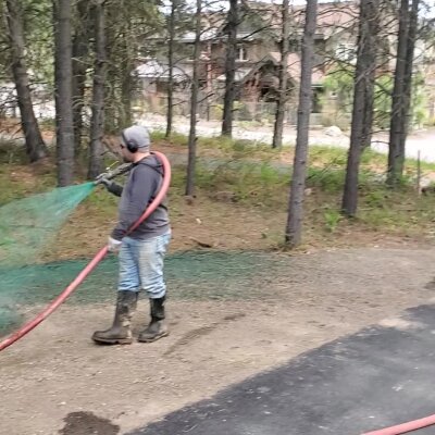 Worker spraying green hydroseed mixture on soil for grass planting.