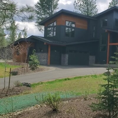 Modern black house with large windows and stone accents in forest setting.