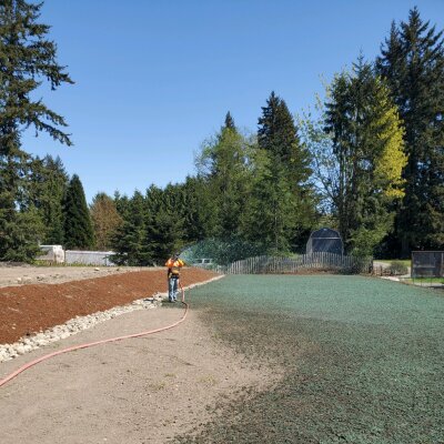 Worker applying hydroseed mixture for erosion control in landscaped area.