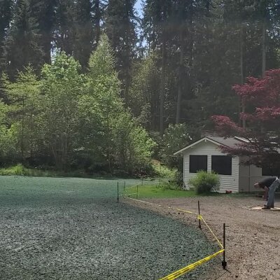Hydroseeding process on lawn near forest with worker and building.