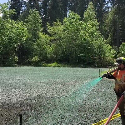 Worker hydroseeding lawn with sprayer in Washington.