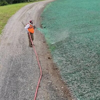 Worker hydroseeding lawn with green slurry through hose.