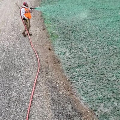 Worker applying hydroseed mixture to soil with hose in Washington state.