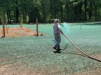 Hydroseeding technician spraying green slurry on lawn in Washington State.