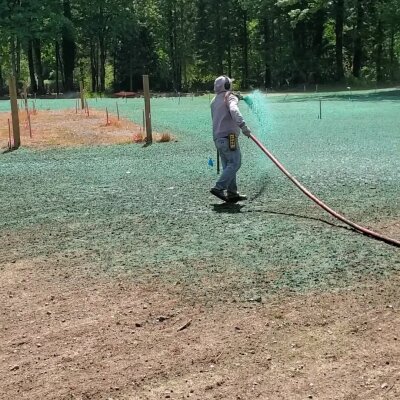 Hydroseeding technician spraying green slurry on lawn in Washington State.