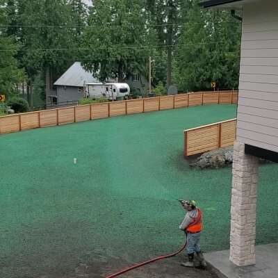 Worker applying hydroseed mixture to lawn in residential area.