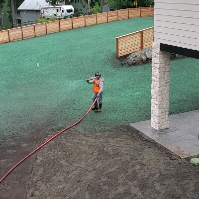 Worker hydroseeding new lawn in residential backyard.