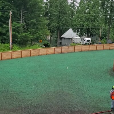 Freshly hydroseeded lawn with wooden fence and worker in Washington.