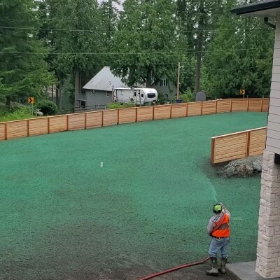 Hydroseeding technician applying green slurry to new lawn in residential area.