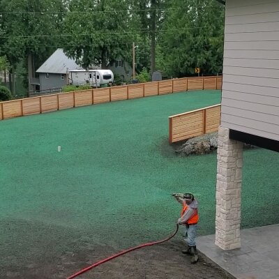 Worker hydroseeding new lawn in residential area.