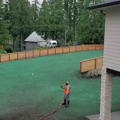 Worker hydroseeding new lawn in residential area.