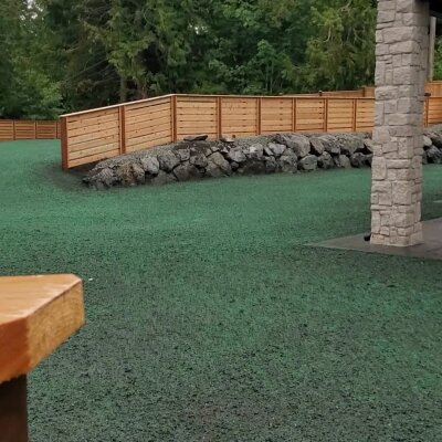 Hydroseeded lawn during installation, wooden fence, and stone column.