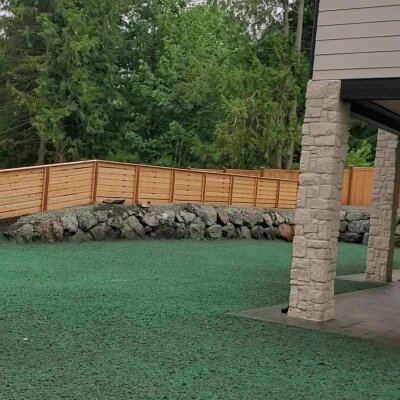 Freshly hydroseeded lawn with stone wall and wooden fence in Washington state.