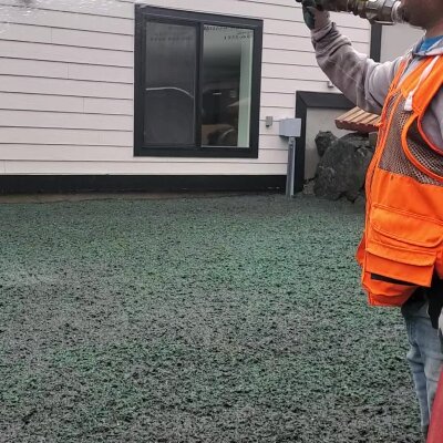 Hydroseeding process by worker near house in Washington State.