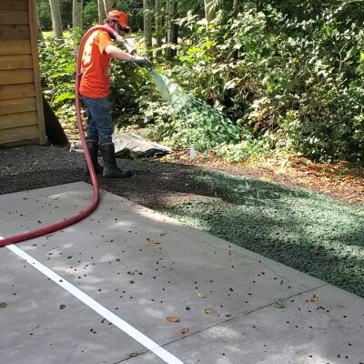 "Hydroseed installer applying mixture on soil near concrete path."