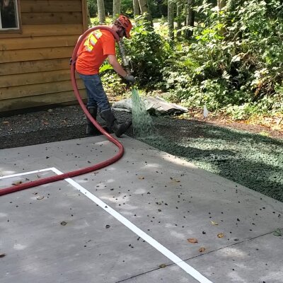 Worker hydroseeding lawn with hose near building.